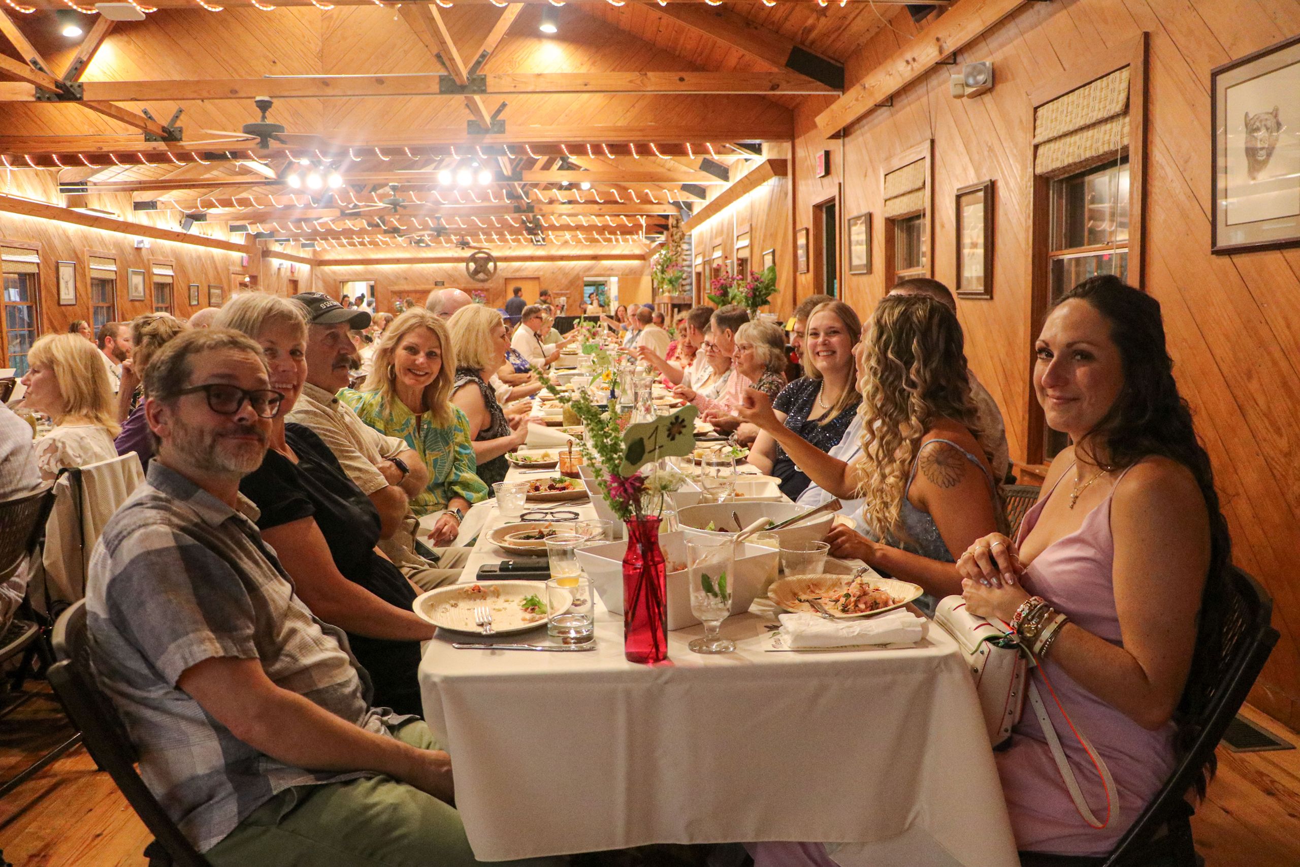 Looking down the long dinner table, guests are smiling and talking as they eat dinner.
