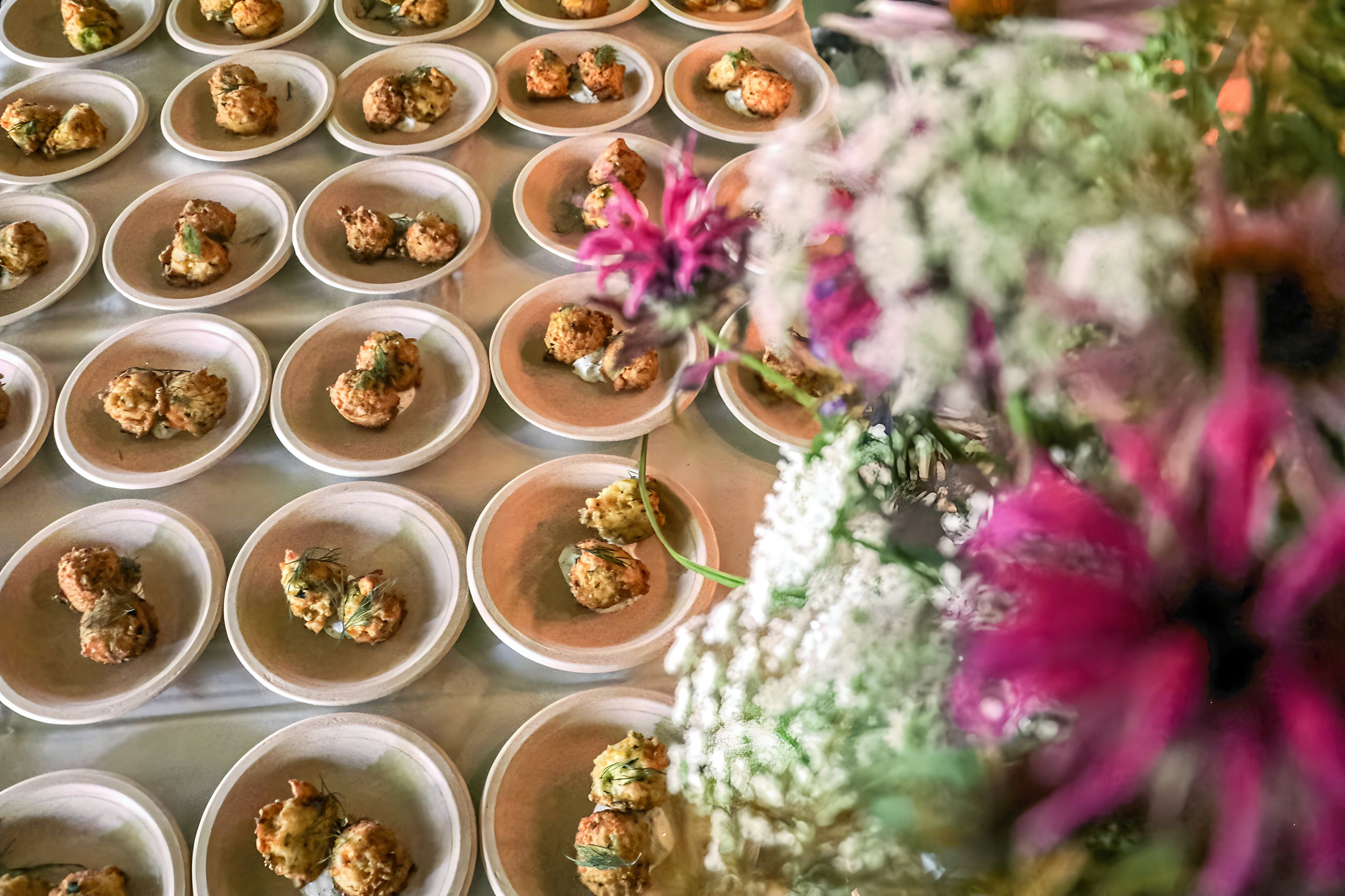 Multiple rows of plates with hors devours and flowers in the foreground on the right.  