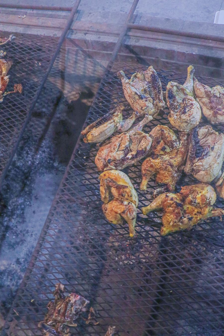 A metal rack of smoked chicken over smoky coals.