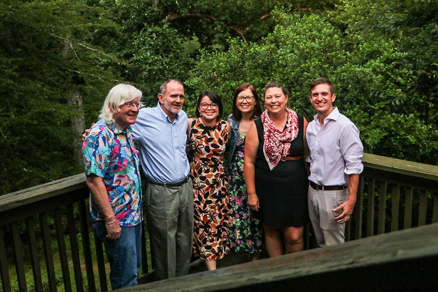 A handful of people who have been involved in UGArden stand arm-in-arm as they smile for a group photo on the deck with trees in the background.