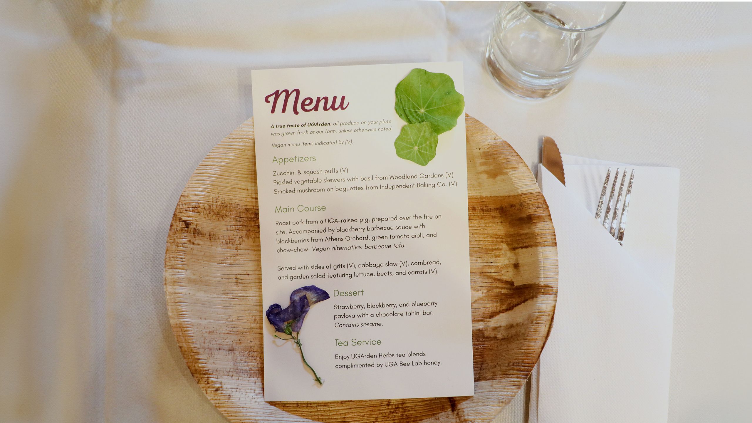 An image of the banquet menu with dried flower petals glued on top. The menu sits on top of a wooden plate with silverware placed to the right.
