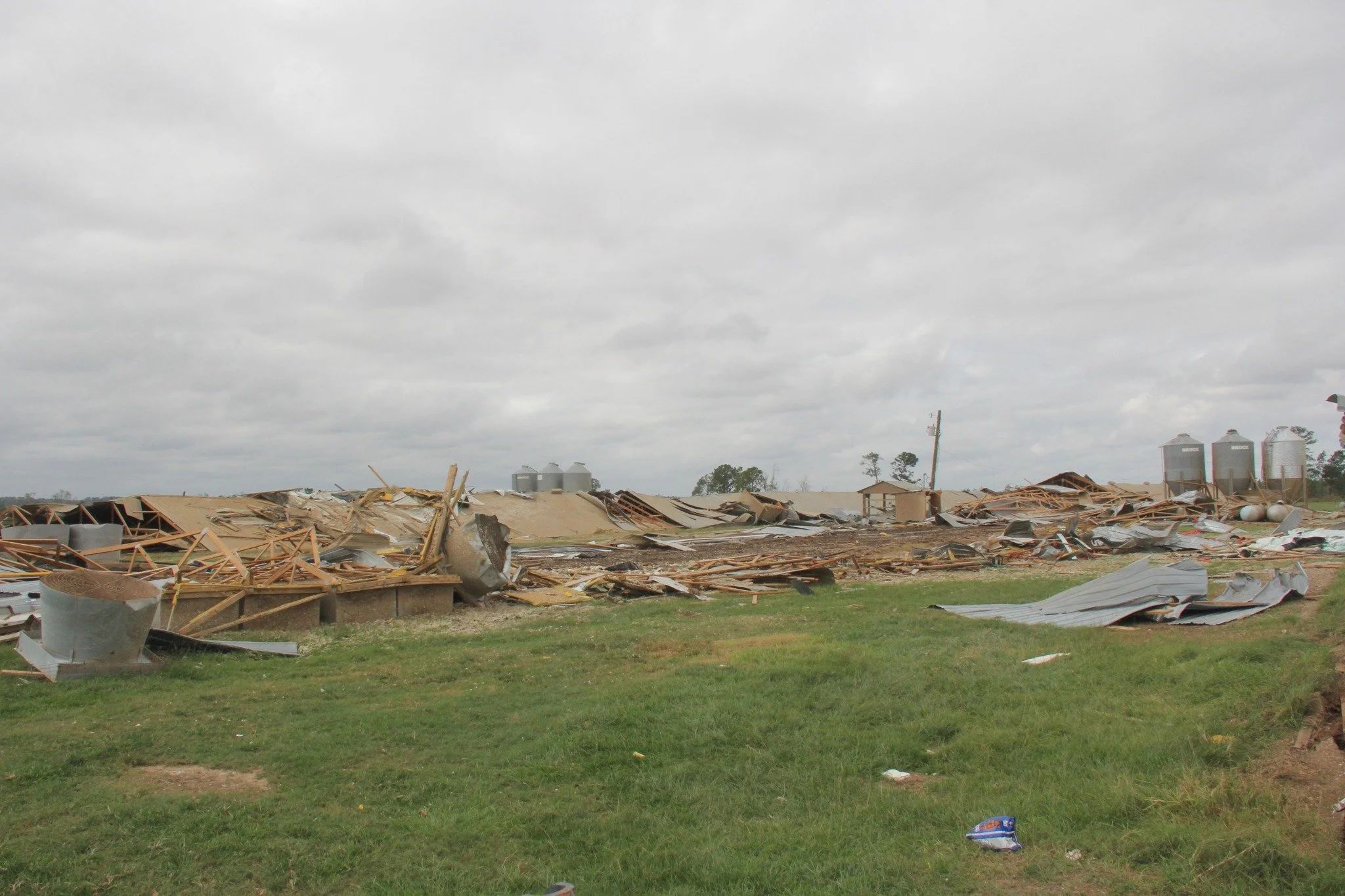 Widespread farm damage with collapsed buildings, scattered debris, and overturned structures under an overcast sky.
