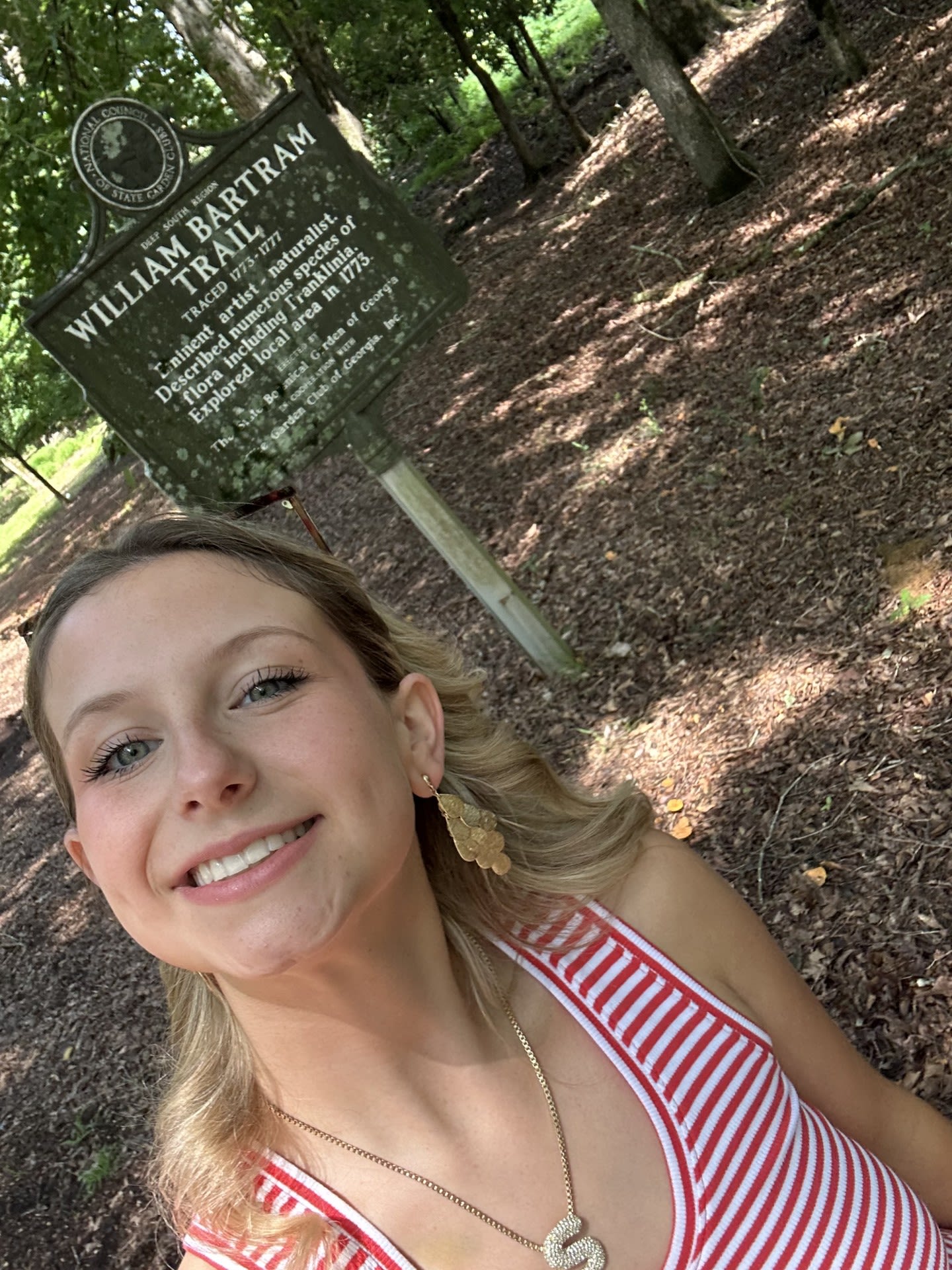 Sydney Fennell, wearing a red and white striped tank top, smiles in front of a marker for William Bartram Trail