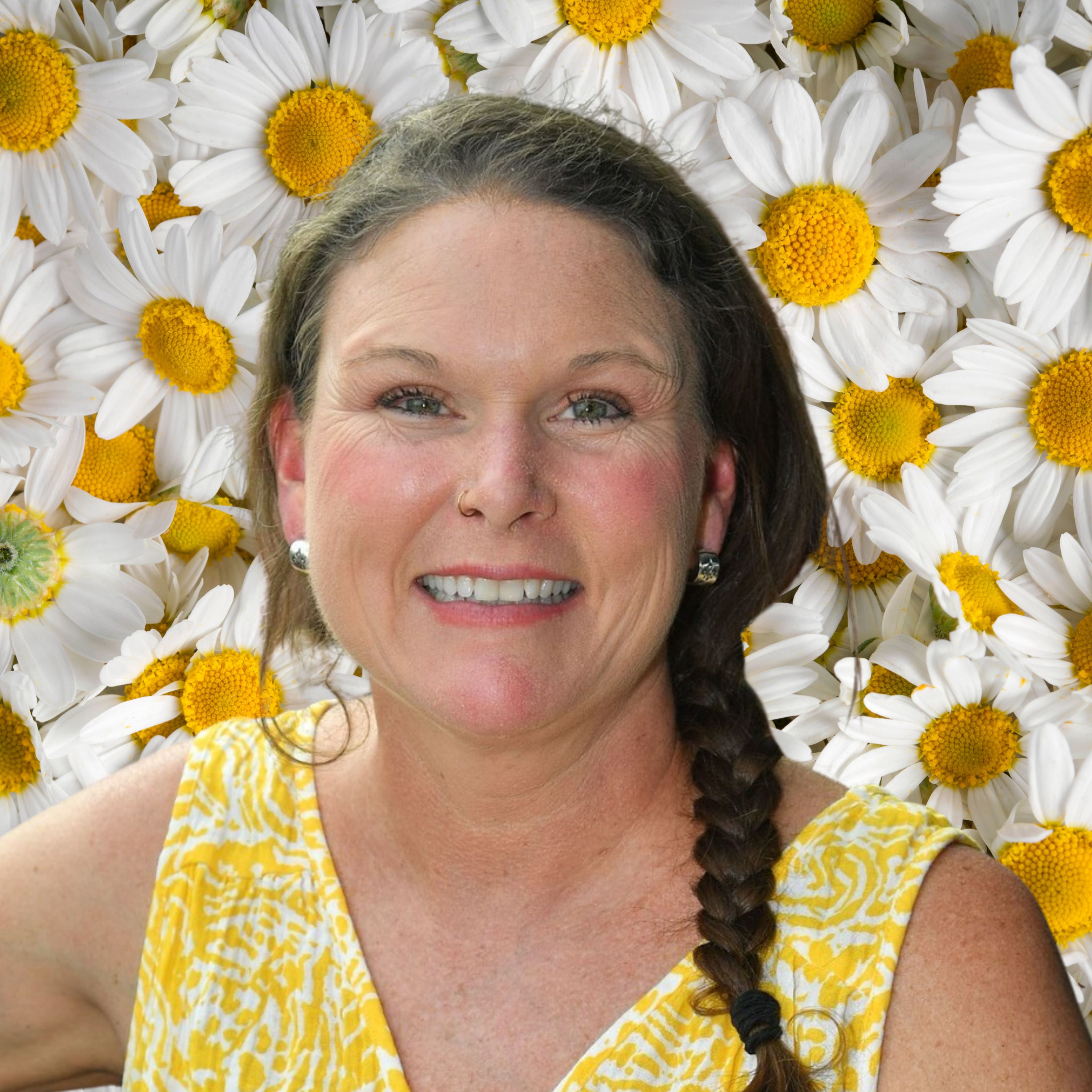 Woman with braided hair and yellow top, smiling in front of daisies.