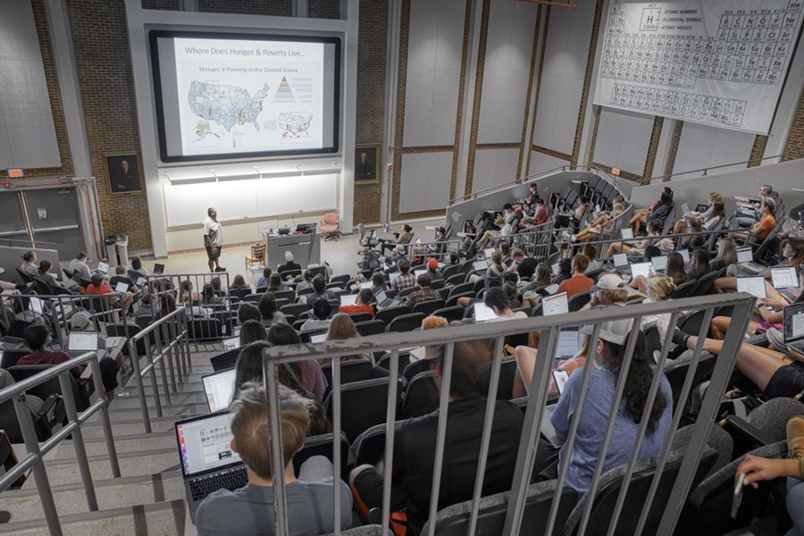 A professor gives a lecture inside a large lecture hall.