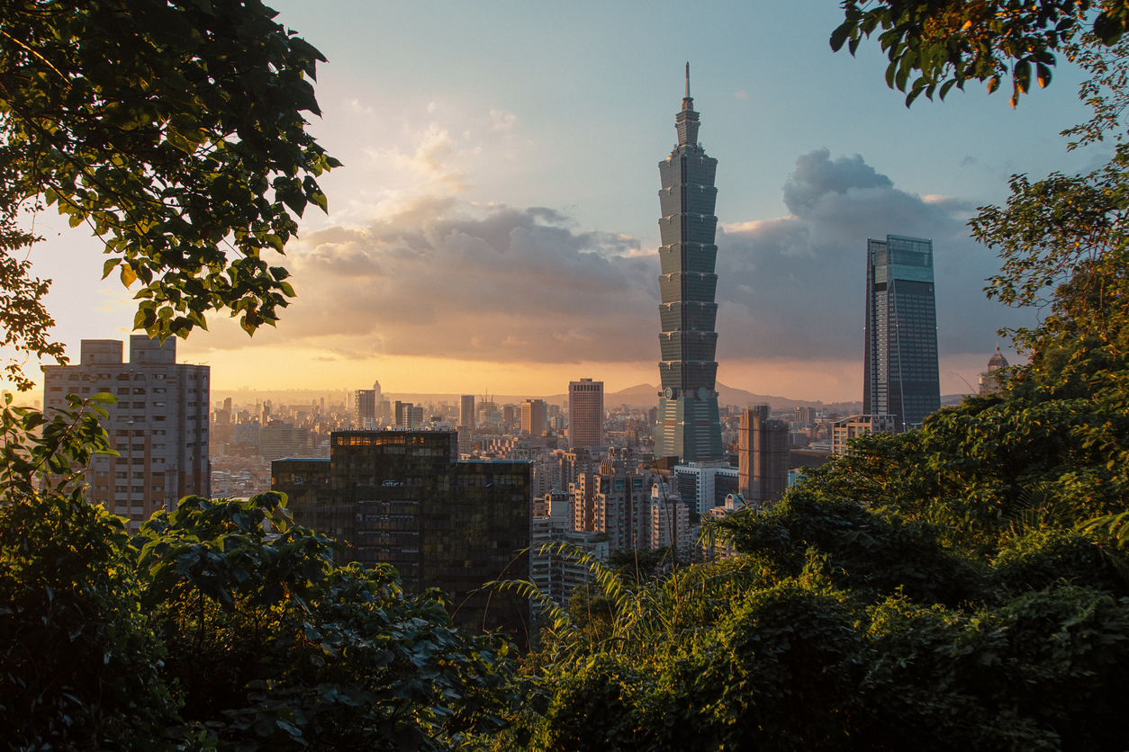 The Taipei skyline glimmers under the golden hour, with skyscrapers framed by foliage