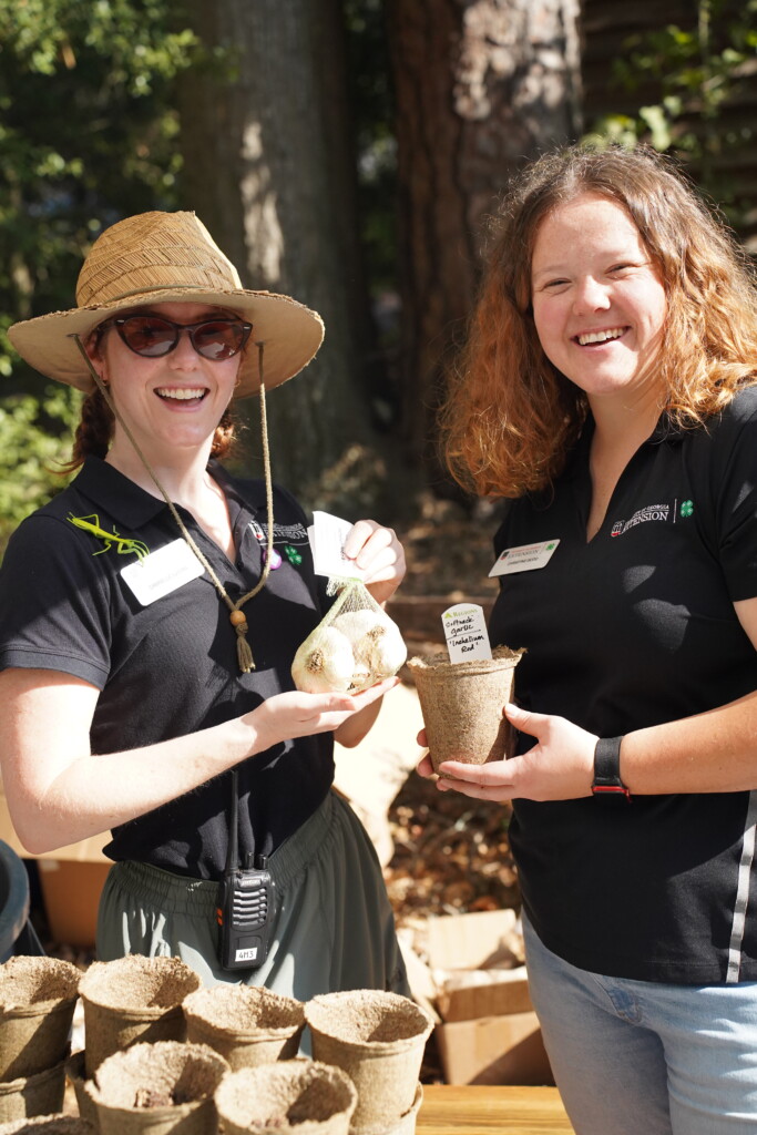 Two UGA Extension educators smile while holding biodegradable pots filled with soil and plant labels during a gardening activity.