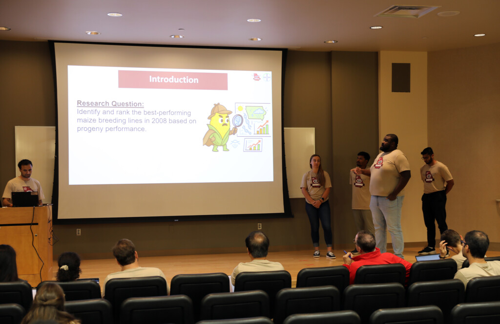 a group of 5 students present a presentation on corn data on a small stage in a room with brown walls