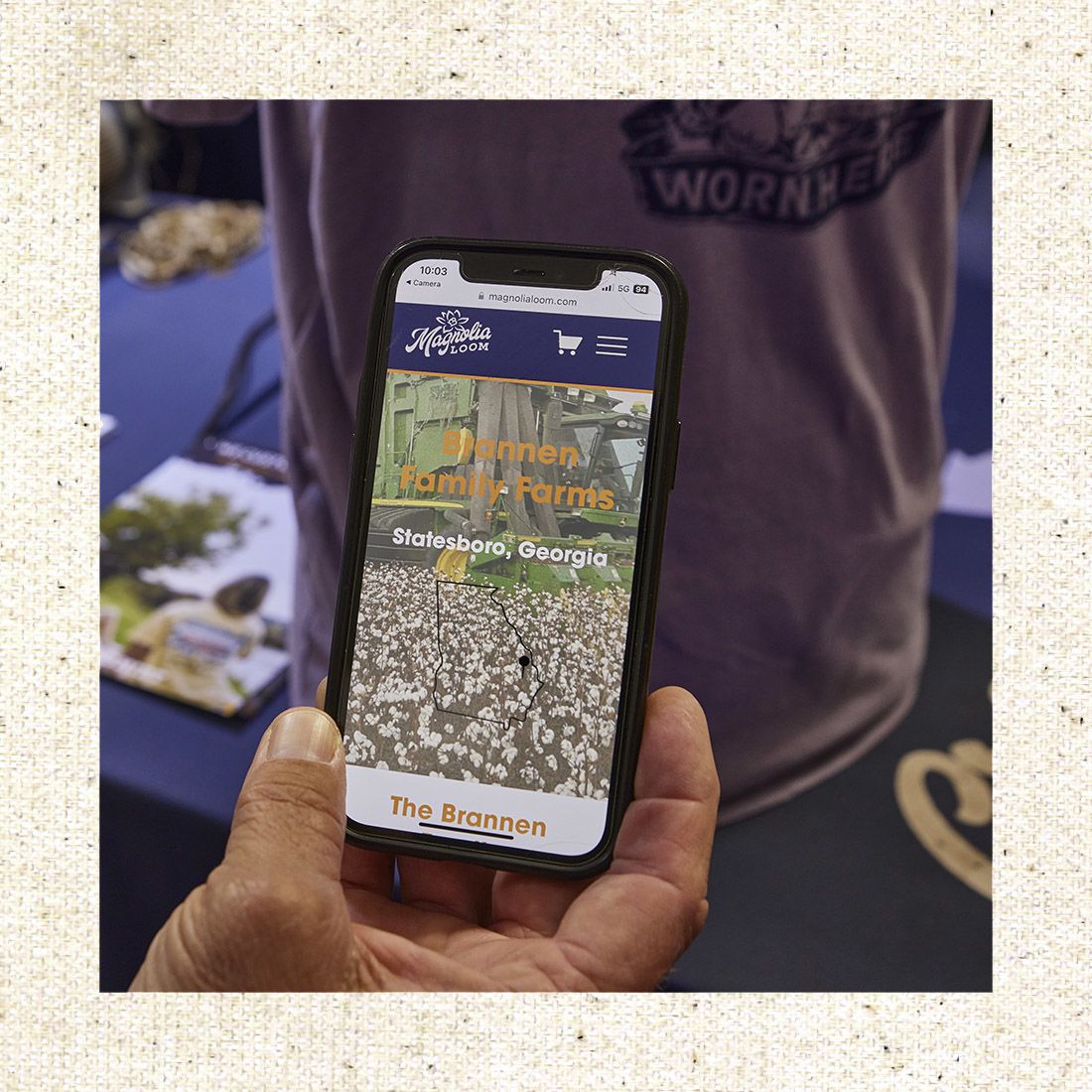 Hand holds a smartphone displaying a website for Brannen Family Farms in Statesboro, Georgia, with a cotton field image.