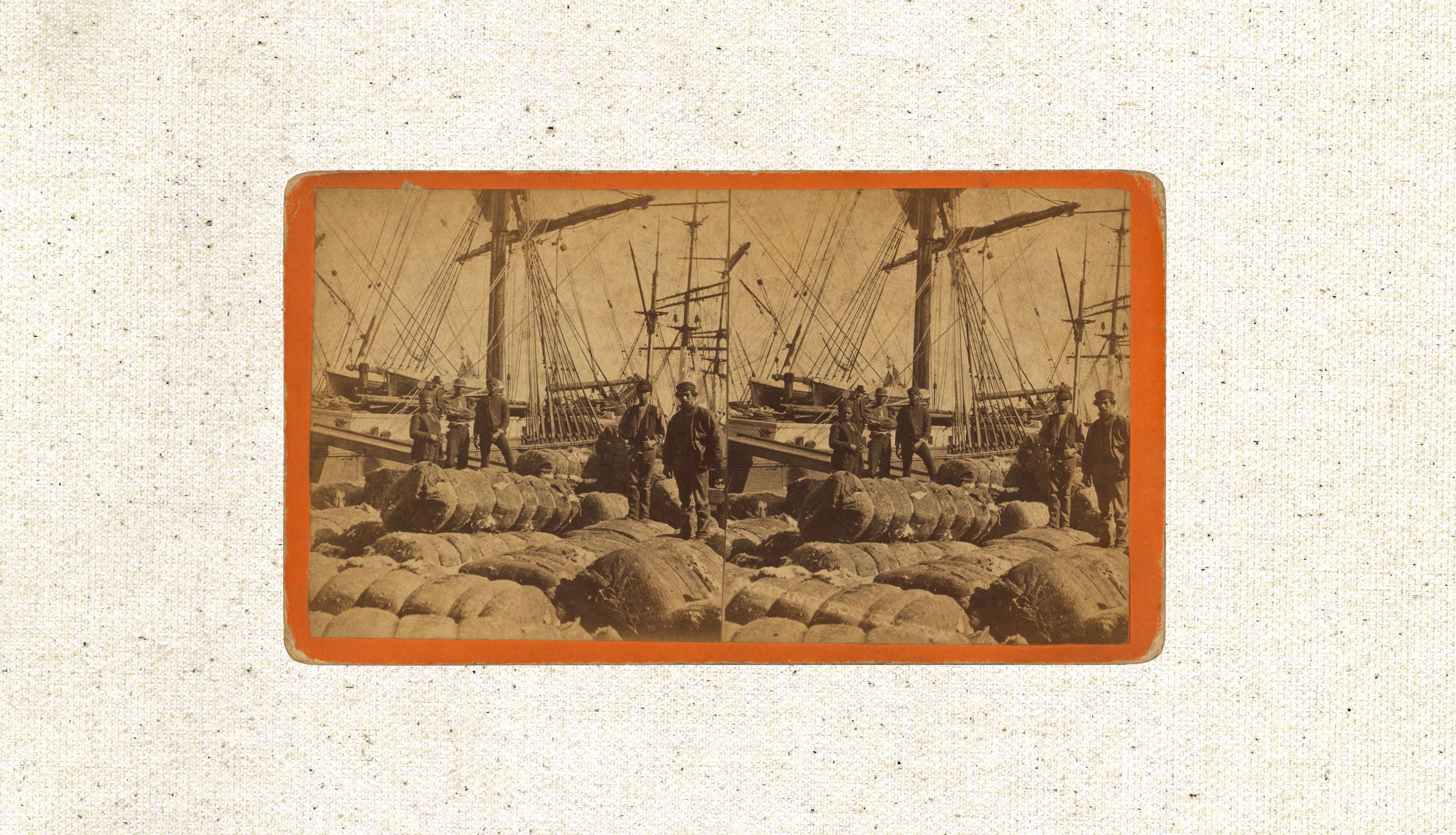 Men stand on a dock beside large cotton bales, with tall ships and masts in the background.