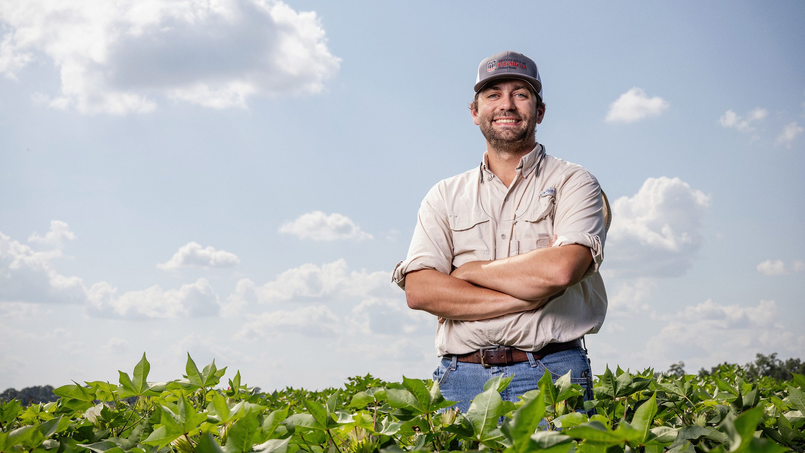 Cotton agronomist Camp Hand stands in a cotton field at UGA-Tifton, smiling with arms crossed under a partly cloudy sky.