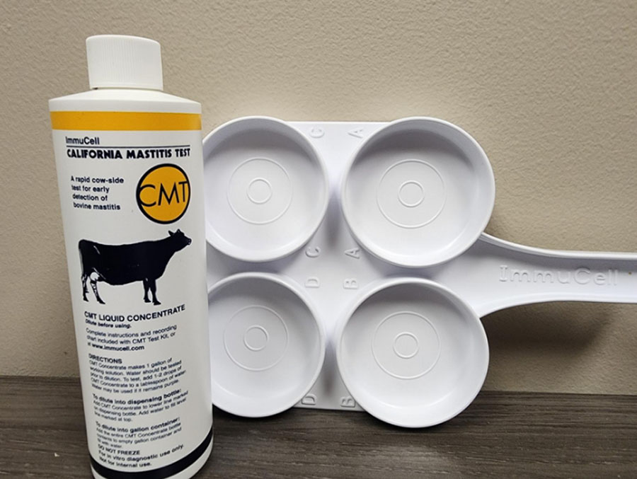 A bottle of mastitis test solution and a CMT paddle are featured in this photo. the paddle has four cups attached to one face.