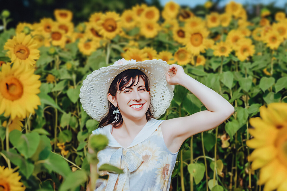 Amy Janvier stands with a sunhat in a field of yellow sunflowers.