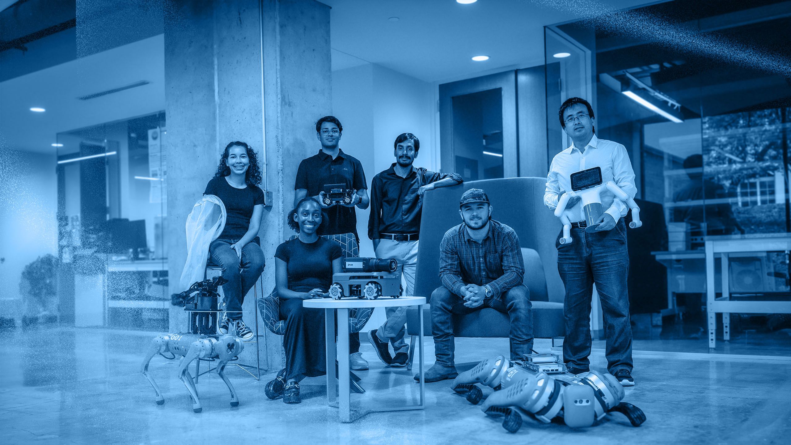 Six people posing in a modern lab space with robotics equipment, including robotic dogs and devices.