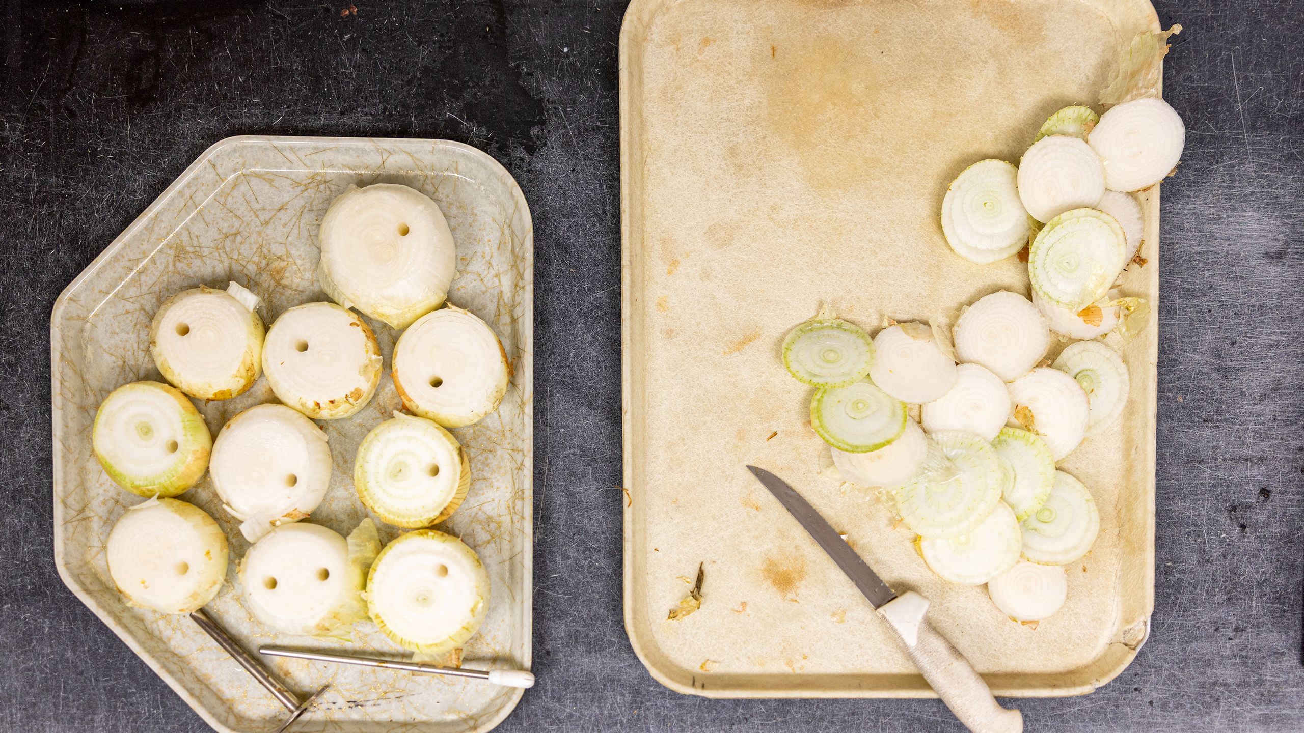 Overhead view of two cutting trays containing onions. On the left, onions with a small core sample removed. On the right, a knife and sliced onion tops. 