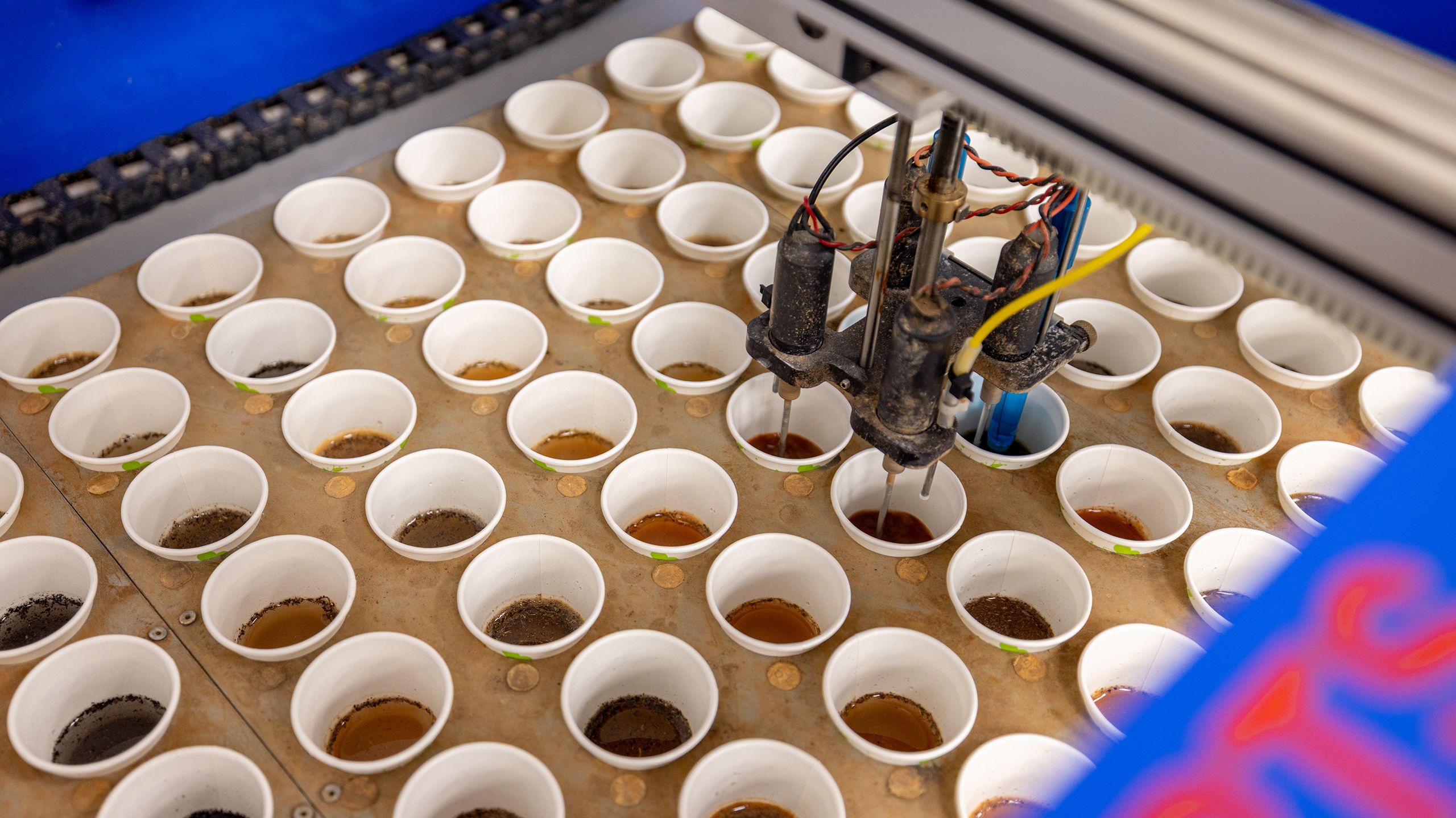 Rows of small sample cups filled with a soil slurry sit in a tray while a machine with multiple probes lowers into them to perform pH analysis