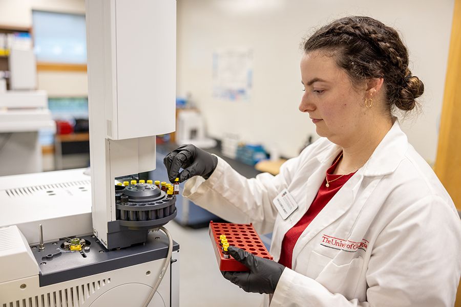 A woman with braided hair places small brown vials into a centrifuge.