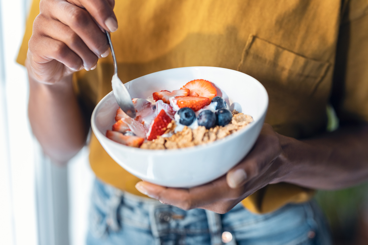 a Black woman holds a bowl of cereal with fruit on top