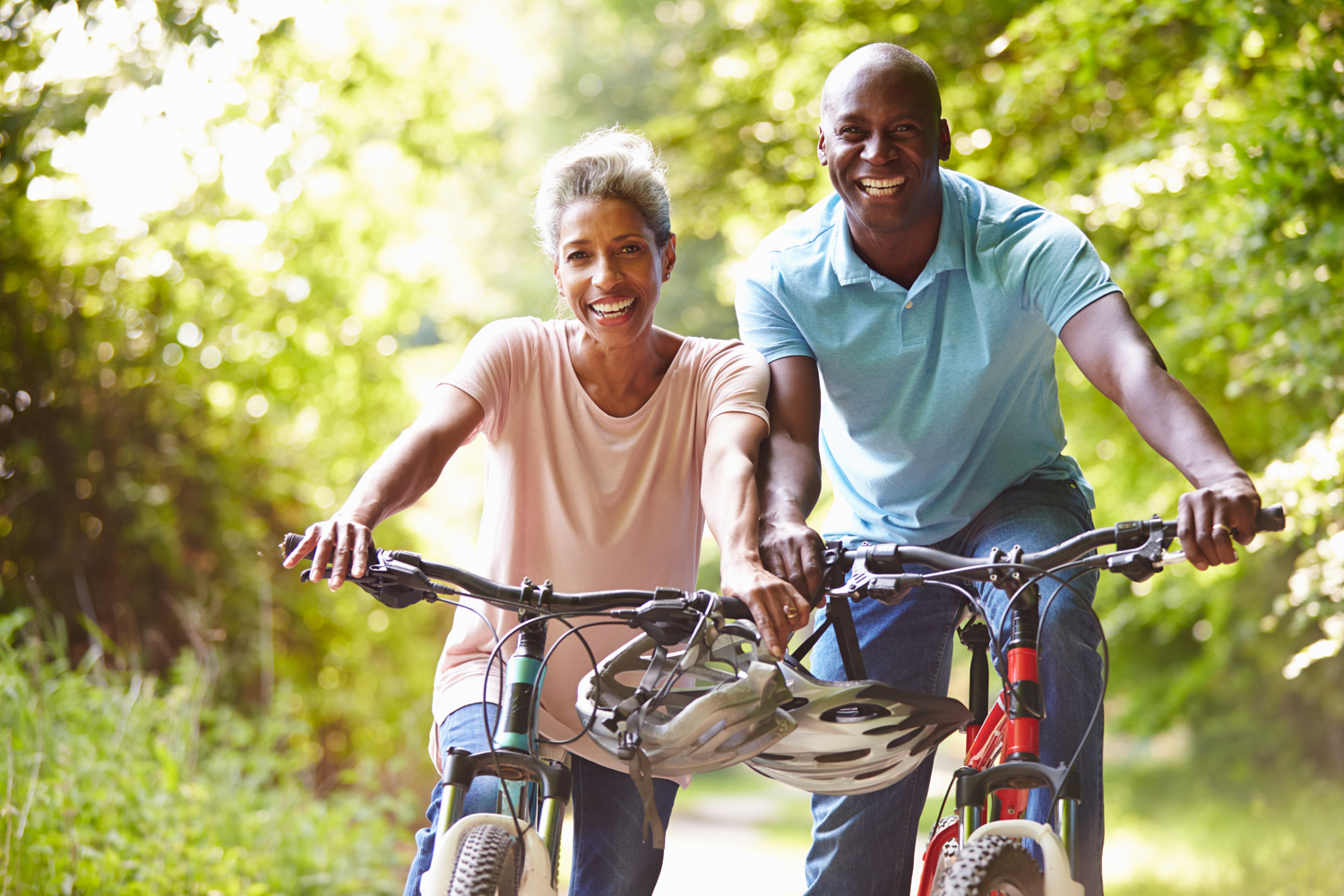 a senior Black couple rides bikes in a forest trail area