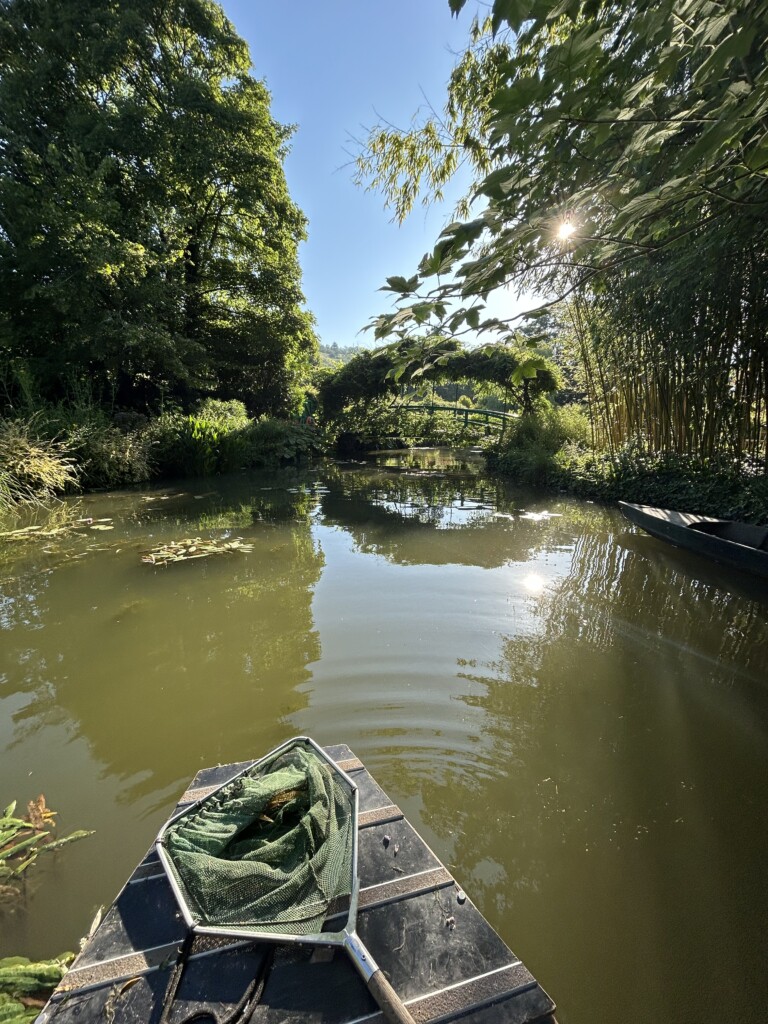 A small boat with a net on the deck floats on a pond at the Monet Gardens.