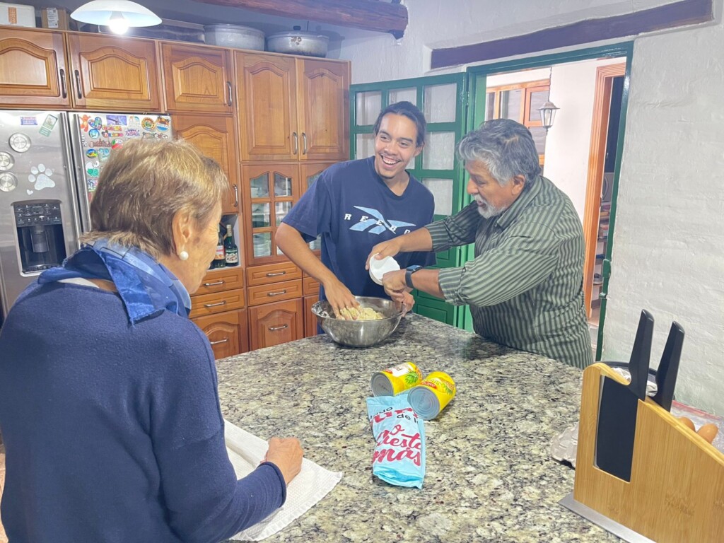 Three people prepare a meal in a home kitchen.