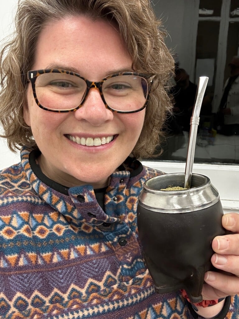A close up selfie of a woman holding a black cup with a silver straw.
