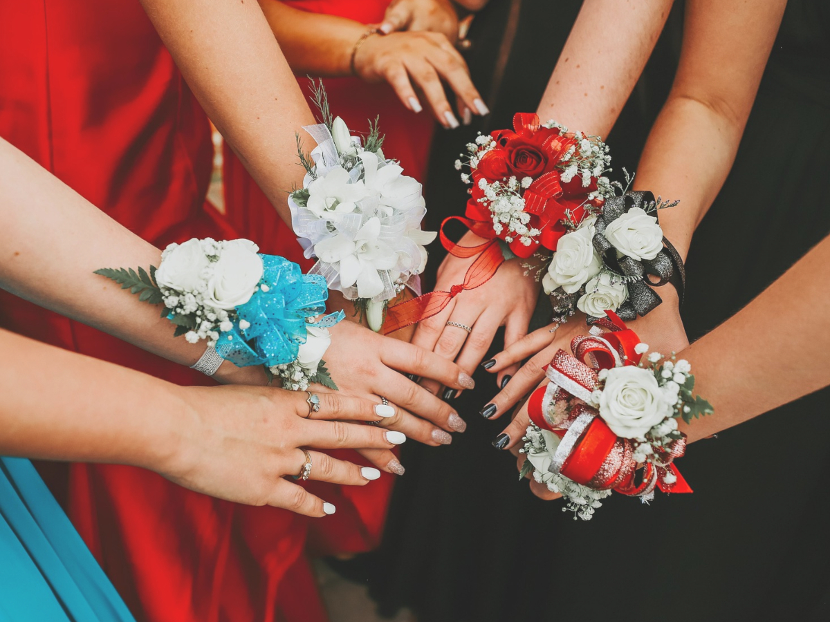 Hands in a circle, each wearing a colorful prom corsage.