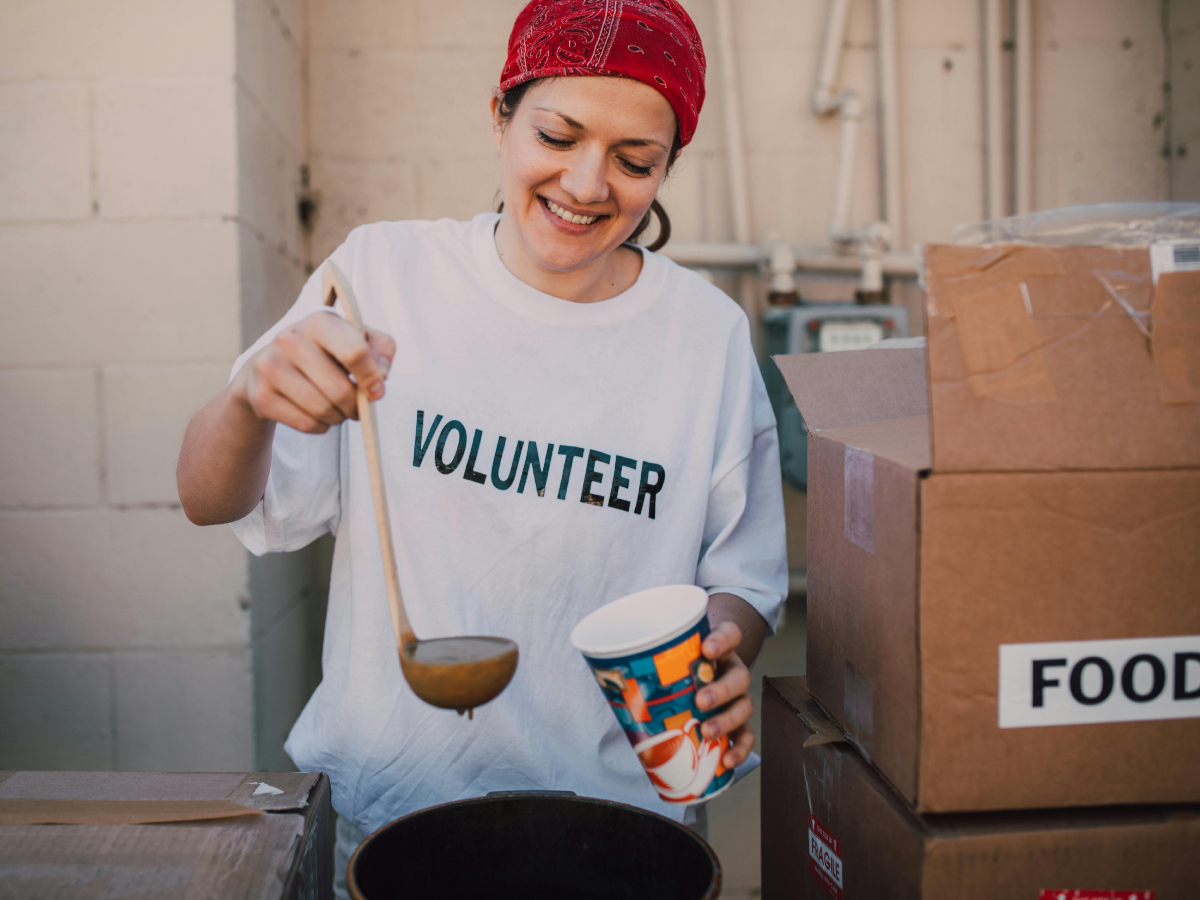 A woman wearing a volunteer tshirt ladles soup into a cup.