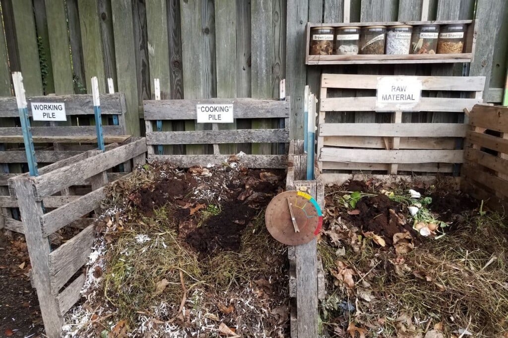 Wooden pallets create a three-bin compost system where food and yard scraps are in various stages of decomposition.