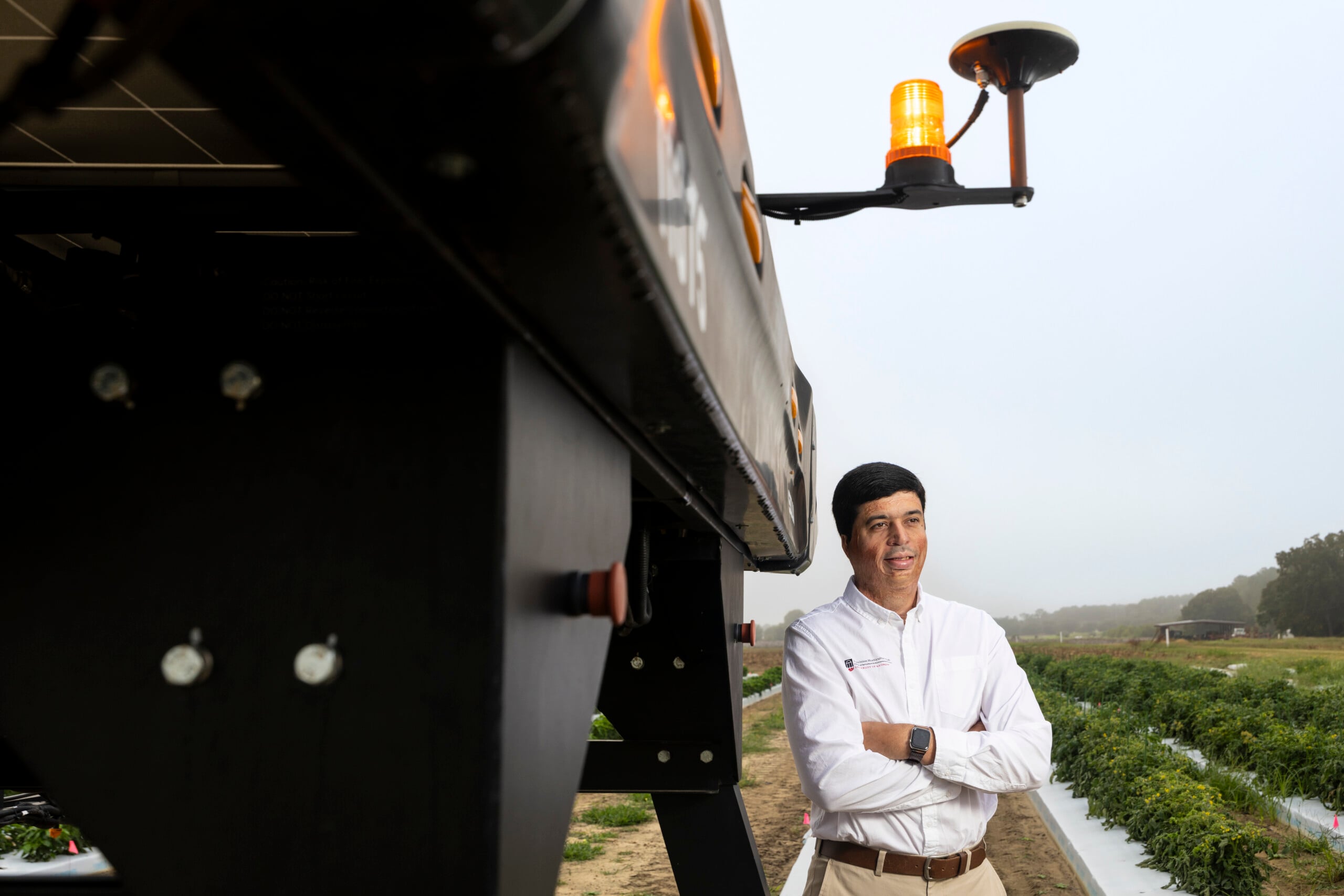 Luan Oliveria smiles and crosses his arms while standing in a field of row crops.