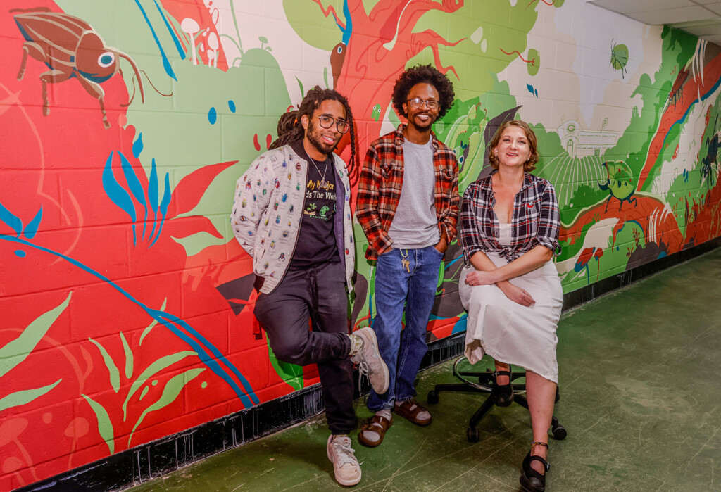 Malcom Peavy, Jamal Hershey Hunter and Kelly Carruthers pose for a photo in front of a colorful mural of insects