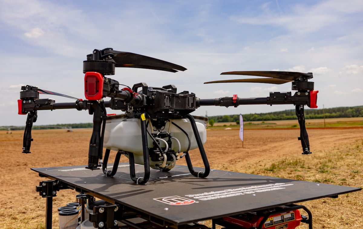 An agricultural drone sits on a robotic platform in the foreground of a recently plowed field.
