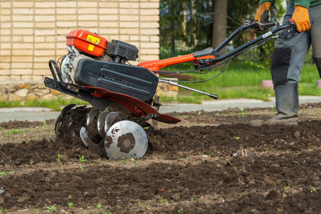a person tills soil near a yellow brick wall