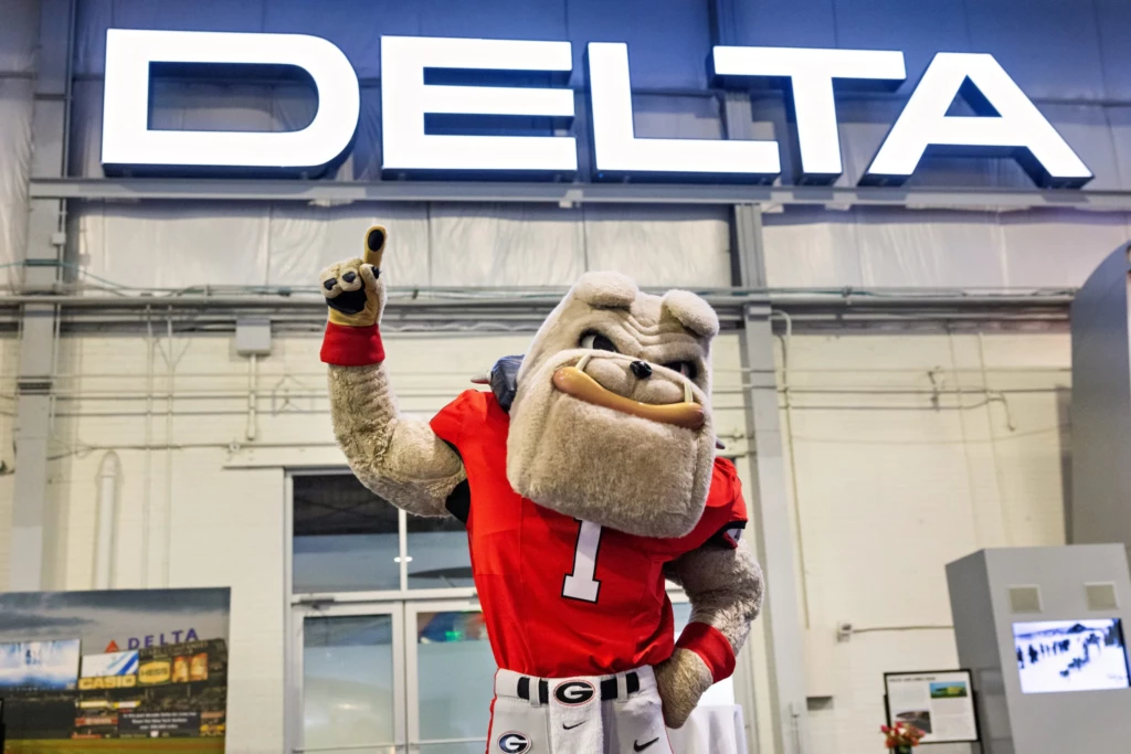 Bulldog mascot makes #1 hand gesture under a glowing Delta logo sign