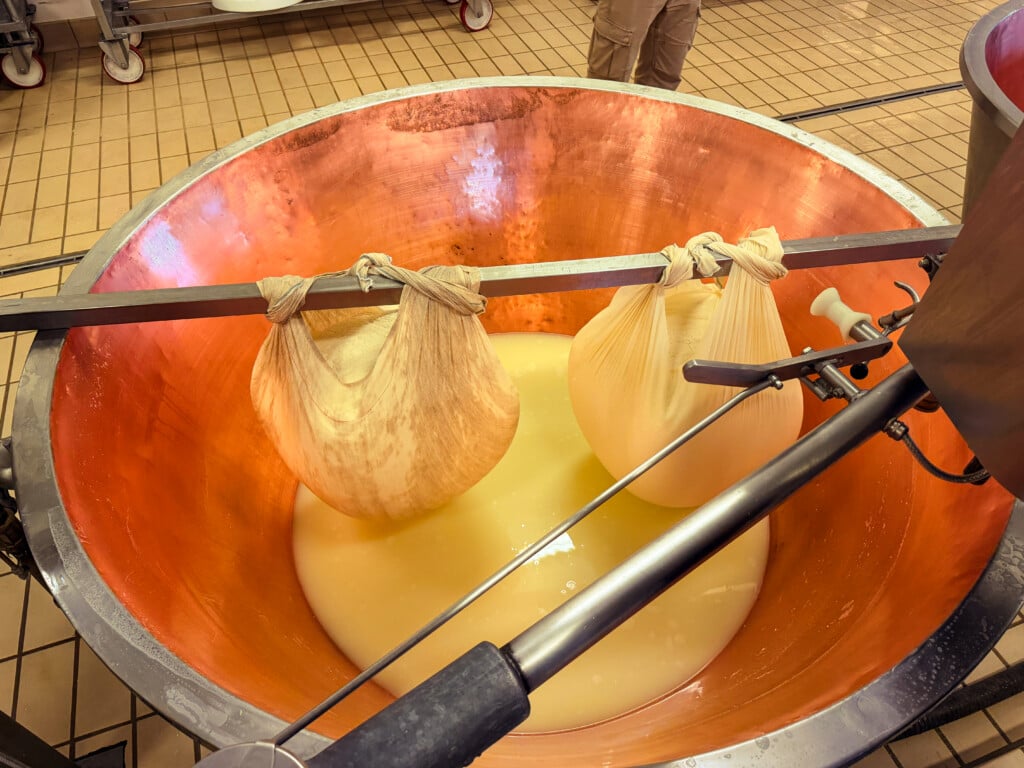 Two bags of milk are hung from a metal rod in a large copper vat, separating the milk whey from the curds that will become cheese. 