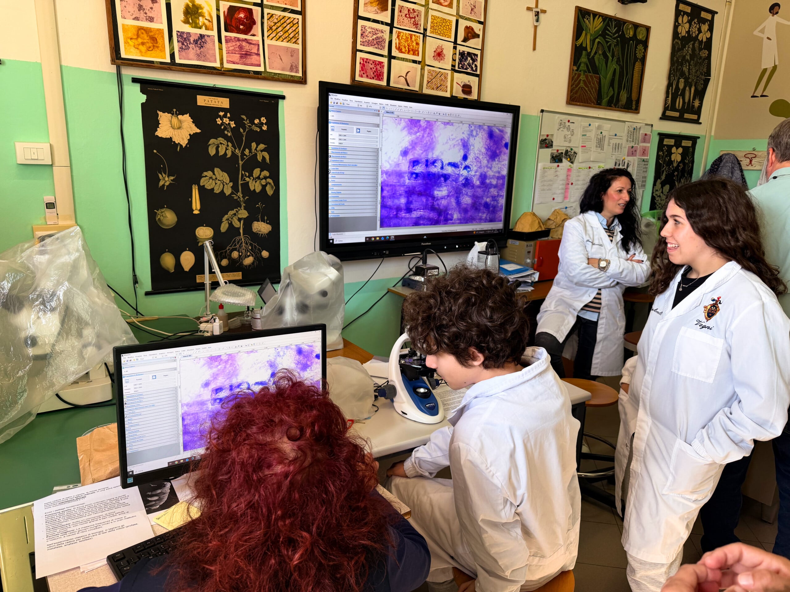 Students wearing lab coats are in a science classroom looking at a computer screen.