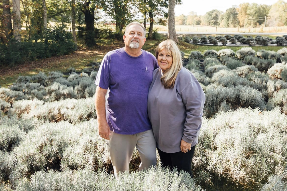 A couple in purple shirts stand in a lavender field