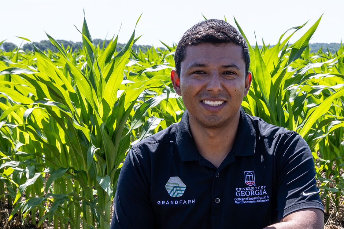 Lenin Rodriguez sits in a corn field on a sunny day.