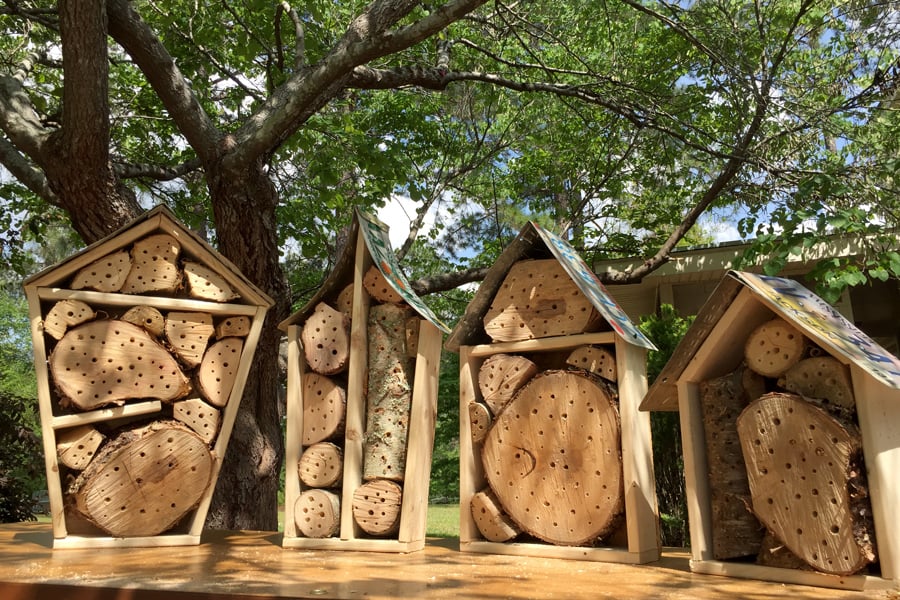 found handmade pollinator nesting boxes are made form tree trunk cuttings and scrap lumber, with a license plate for each roof