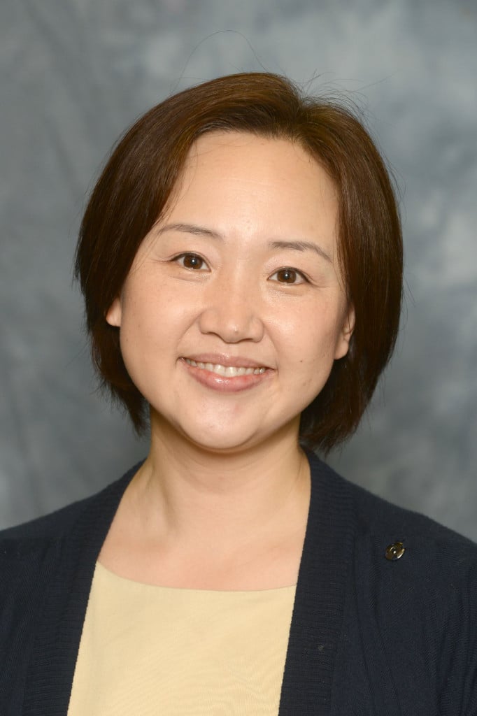 A professional headshot of a smiling woman in a blue blazer and pale yellow shirt.