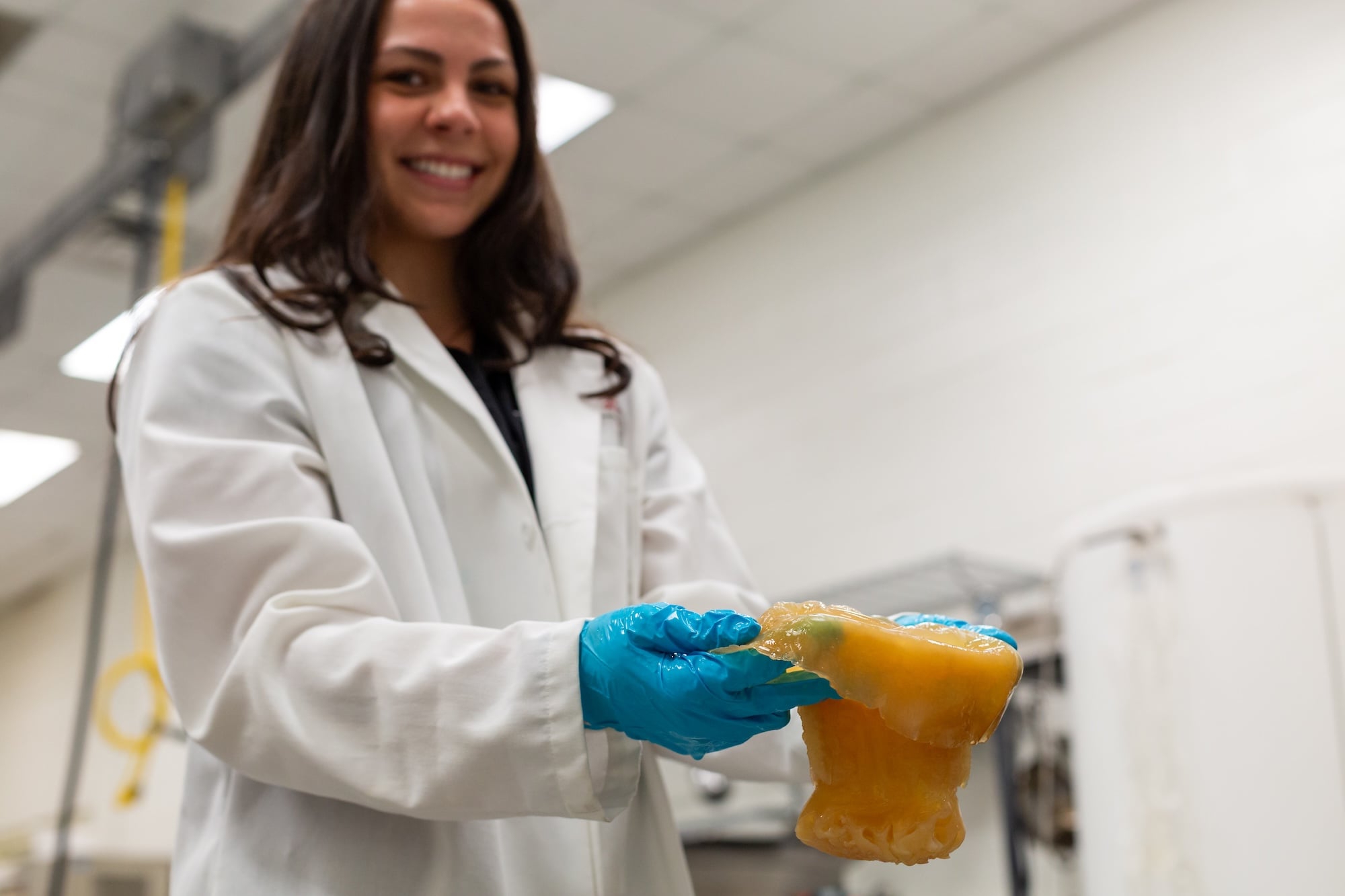 Gina Fimiano wears a lab coat and gloves stands in a processing facility and holds a cannonball jellyfish.