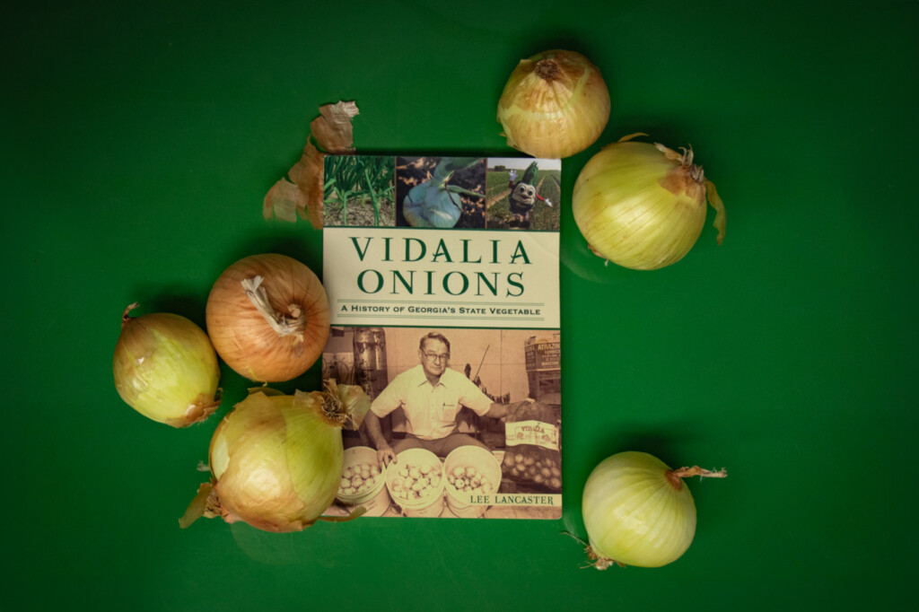 Lee Lancaster's "Vidalia Onions: A History of Georgia's State Vegetable" book on a green table surrounded by Vidalia onions