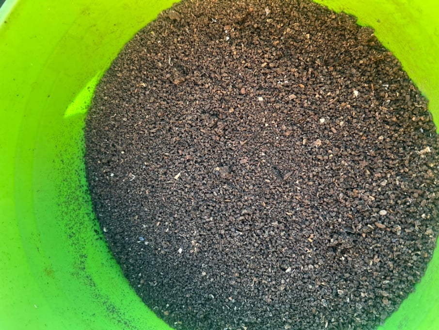a closeup of the inside of a green bucket filled with dark granules of compost