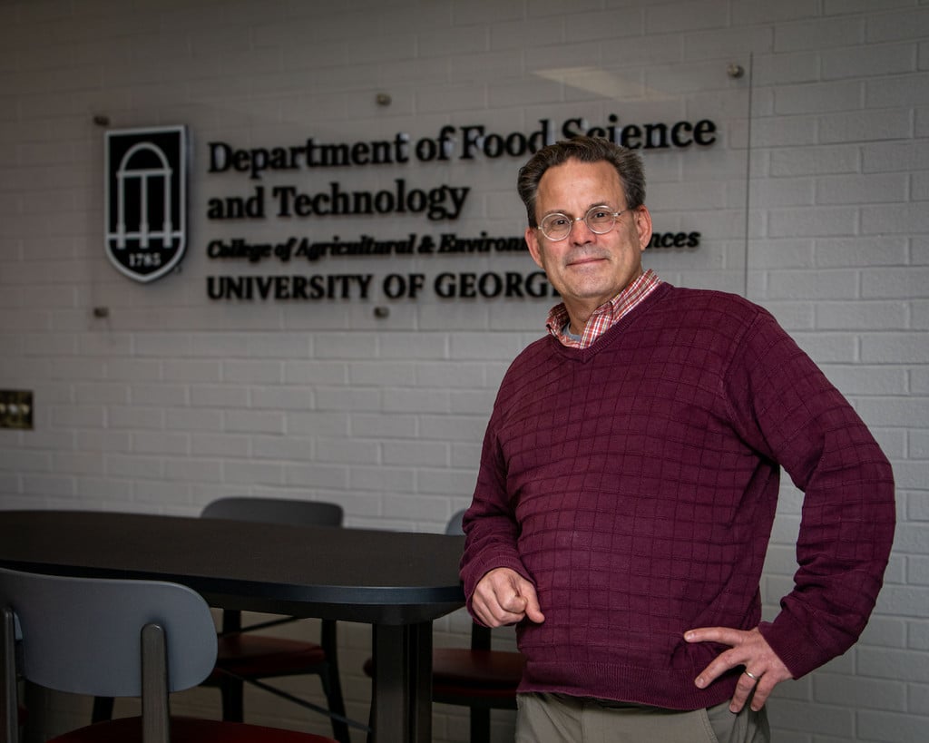Jim Gratzek stands indoors, in front of a logo sign of UGA Department of Food Science and Technology