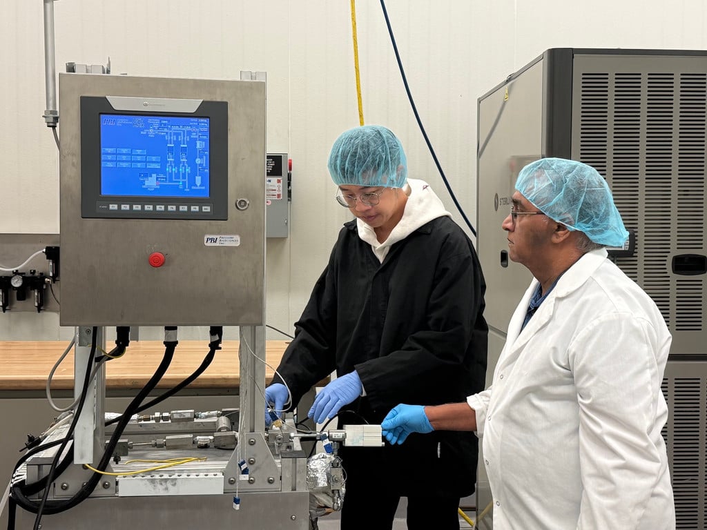 UGA food engineering researcher V.M. Balasubramaniam, right, and postdoctoral researcher Hetian Hu, left, wearing protective clothing, hairnets and blue gloves, examine high-pressure processing equipment in a food science laboratory.