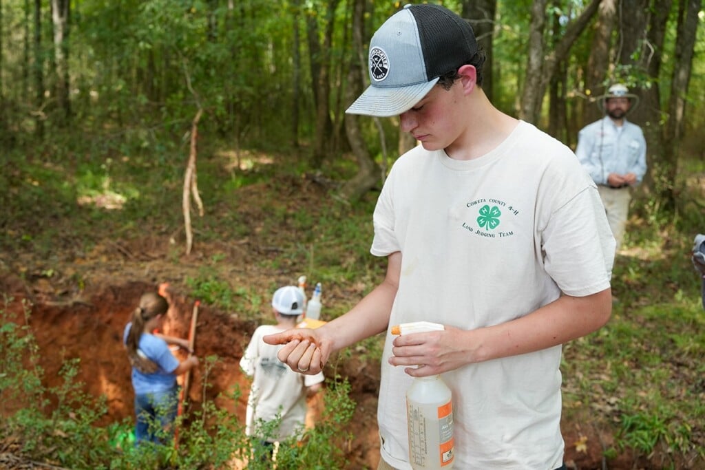 A young man in a white t-shirt and black and white trucker cap examines a handful of soil