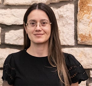 A woman with long straight brown hair wearing glasses and a black top
