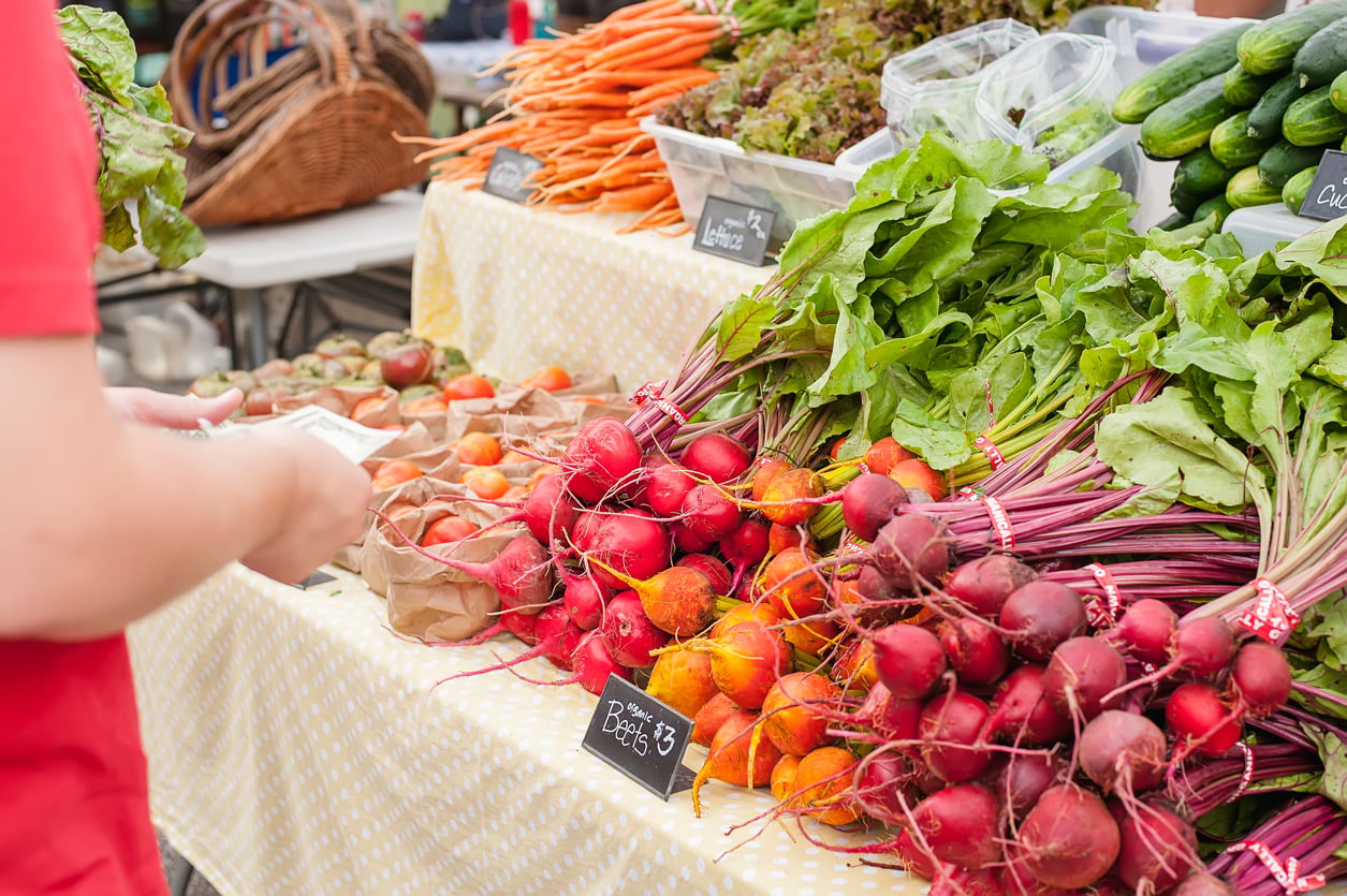 Fresh vegetables, including beets, carrots and leafy greens, displayed at an outdoor farmers market.